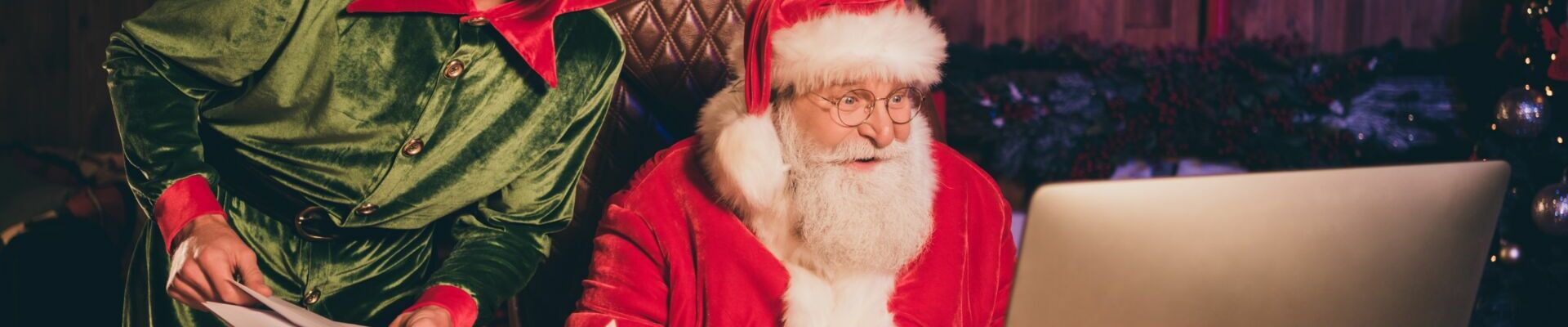 photographie d'un lutin joyeux à côté du père noel, tous les deux en train de trier des lettres et des emails adressés au Pôle Nord