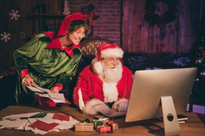 photographie d'un lutin joyeux à côté du père noel, tous les deux en train de trier des lettres et des emails adressés au Pôle Nord