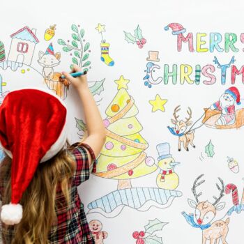 une enfant avec un bonnet de père noël dessine des dessins de Noël