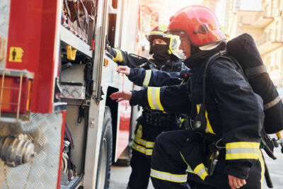 Photo représentant 2 sapeurs pompiers se préparant à une intervention, à côté d'un camion